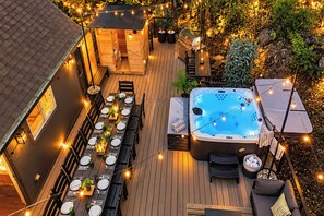 Un jacuzzi rodeado por una terraza con asientos exteriores y luces colgantes.