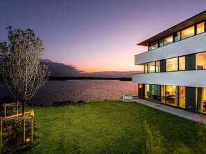 Ein modernes, zweistöckiges Gebäude mit großen Fenstern, einem gepflegten Rasen und Blick auf das Wasser.