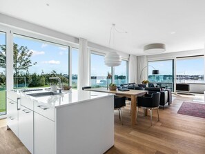 Une cuisine moderne dotée d’un grand îlot central, d’un coin repas avec des chaises et de grandes fenêtres offrant une vue sur l’extérieur.