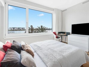 Une chambre d’hôtel moderne dotée d’un grand lit, d’un téléviseur à écran plat, d’un bureau et offrant une vue sur un plan d’eau.