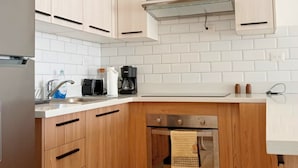 Cozinha moderna com armários de madeira clara, geladeira de aço inoxidável, forno embutido e máquina de café sobre a bancada.
