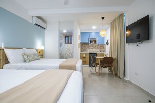 Habitación de hotel con dos camas, kitchenette, zona de comedor y televisor montado en la pared.