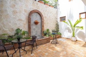 An outdoor patio area with a stone wall, a tiled wall with a decorative arch, and potted plants.