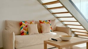 Uma sala de estar moderna com um sofá, uma mesa de centro e uma escada com guarda-corpo de vidro.