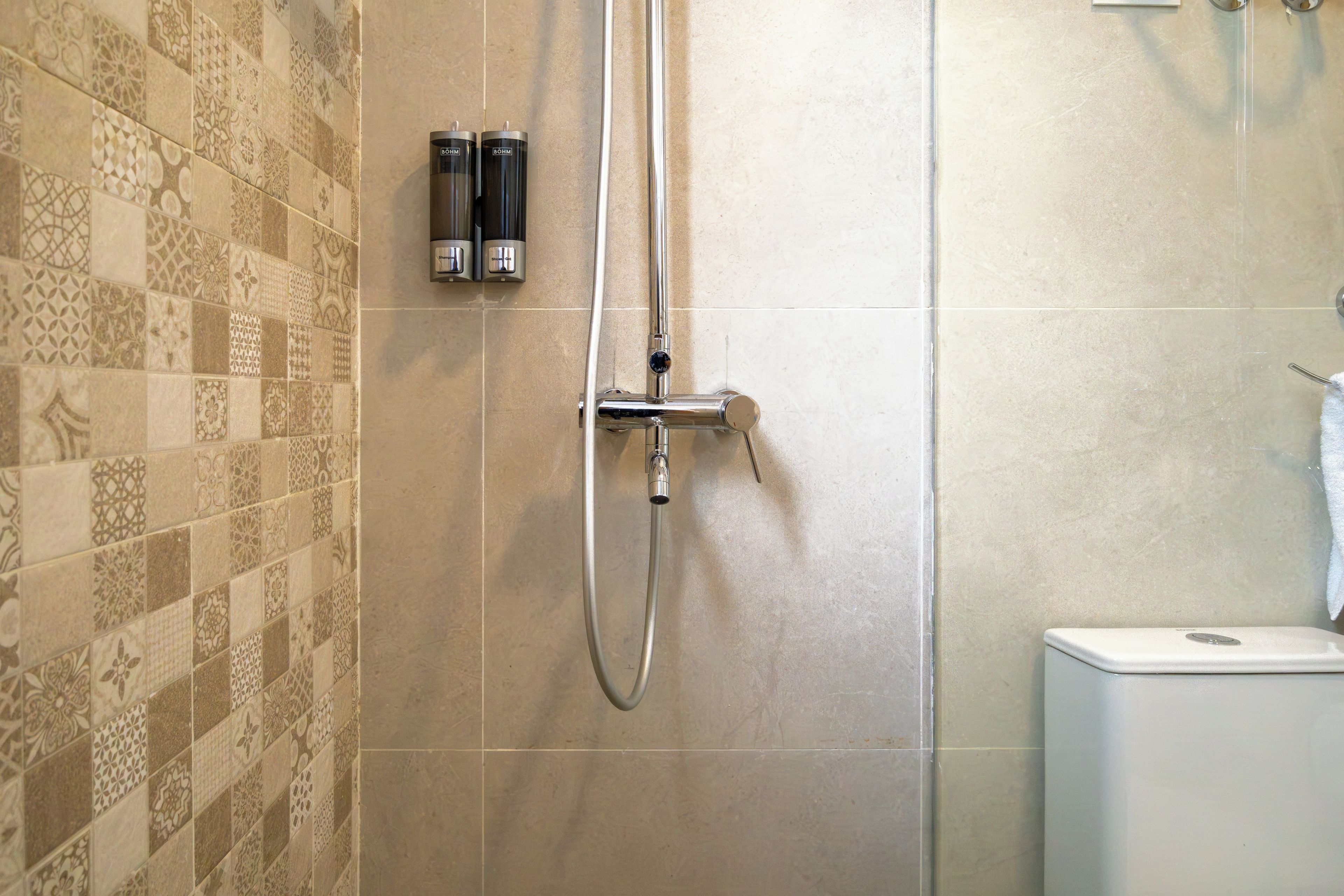 A shower area with a wall-mounted faucet and a handheld showerhead.