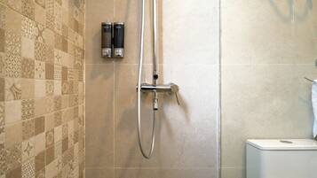 A shower area with a wall-mounted faucet and a handheld showerhead.