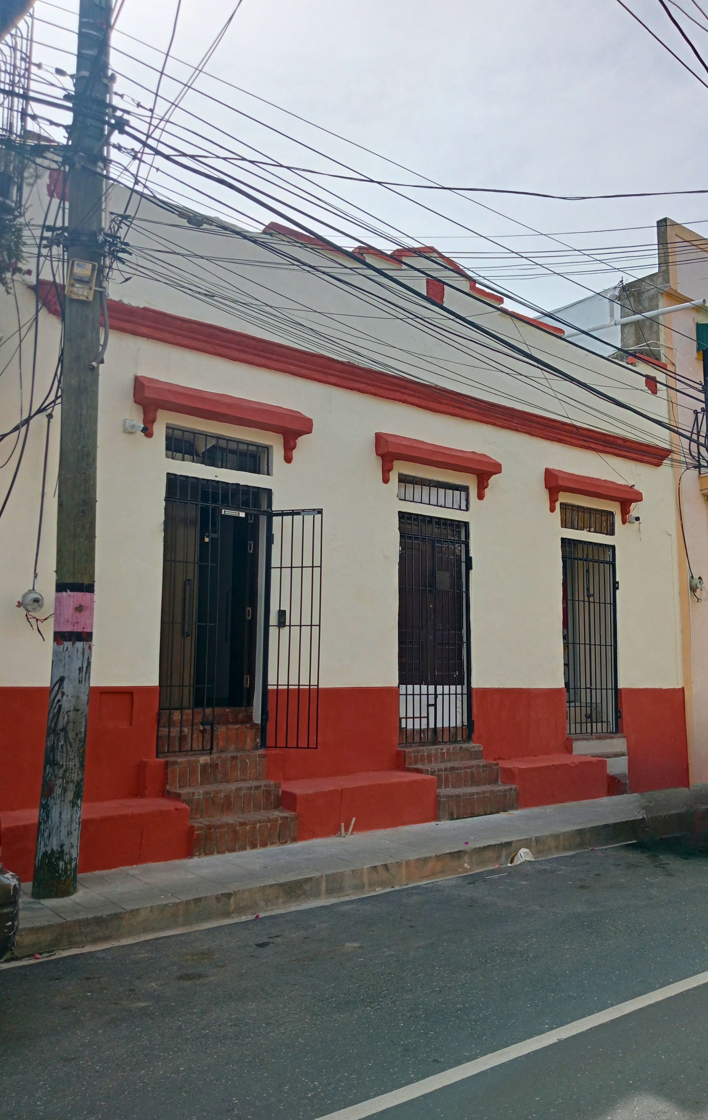 Un edificio con fachada roja y blanca, dos entradas protegidas por rejas y una escalera que lleva a la entrada.