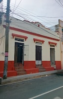 Un edificio con fachada roja y blanca, dos entradas protegidas por rejas y una escalera que lleva a la entrada.
