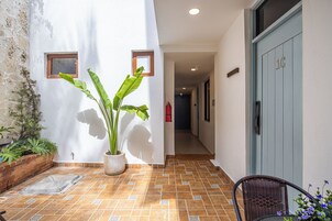 Un pasillo estrecho con piso de baldosas, una planta en maceta y una puerta con placa de número.