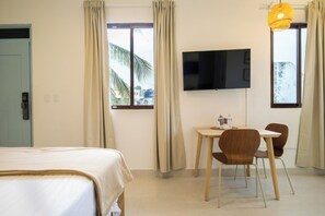 Habitación de hotel con cama, escritorio con dos sillas, televisor de pantalla plana y ventana con cortinas.