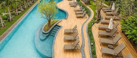 A pool area with a curved design, surrounded by lounge chairs and umbrellas, and a small waterfall feature.