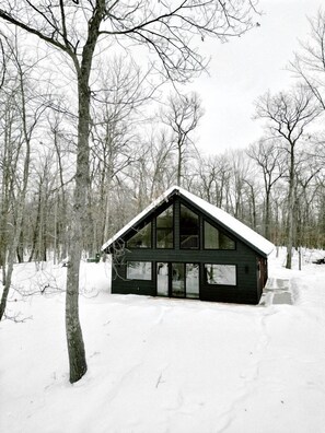 A cabin with a steep roof, large windows, and a snow-covered ground.