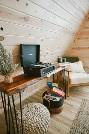 A cozy room with a wooden ceiling, a black Crosley radio on a wooden table, a woven pouf, and a basket of books. - Tranquil Cabin Escape with Private Sauna & Kayak Fun in Mission Township, Minnesota (Mission Township)
