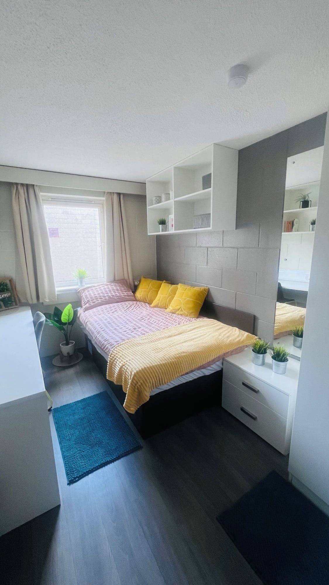 A modern bedroom with a bed, bedside tables, a desk, and a window.