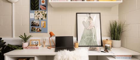A well-organized workspace with a laptop, framed artwork, and a bulletin board with photos and notes.