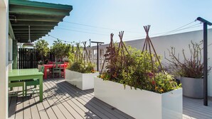 Eine Dachterrasse mit Holzdeck, einer überdachten Sitzgelegenheit und Pflanzkästen mit unterschiedlichen Pflanzen.
