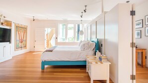Ein modernes Schlafzimmer mit einem großen Bett, einem Nachttisch, einem Fernseher und einer Tür zu einem weiteren Raum.