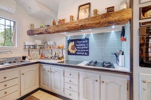 Una cocina con armarios blancos, un estante de madera con vigas y un protector contra salpicaduras de azulejos, además de un cartel con una frase motivadora.