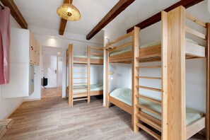 A room with bunk beds, wooden flooring, a hanging light fixture, and a door with a towel hanging on it.