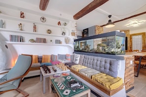 A living room with a sofa, a coffee table with chess and Go sets, a fish tank, and a bookshelf with various items.