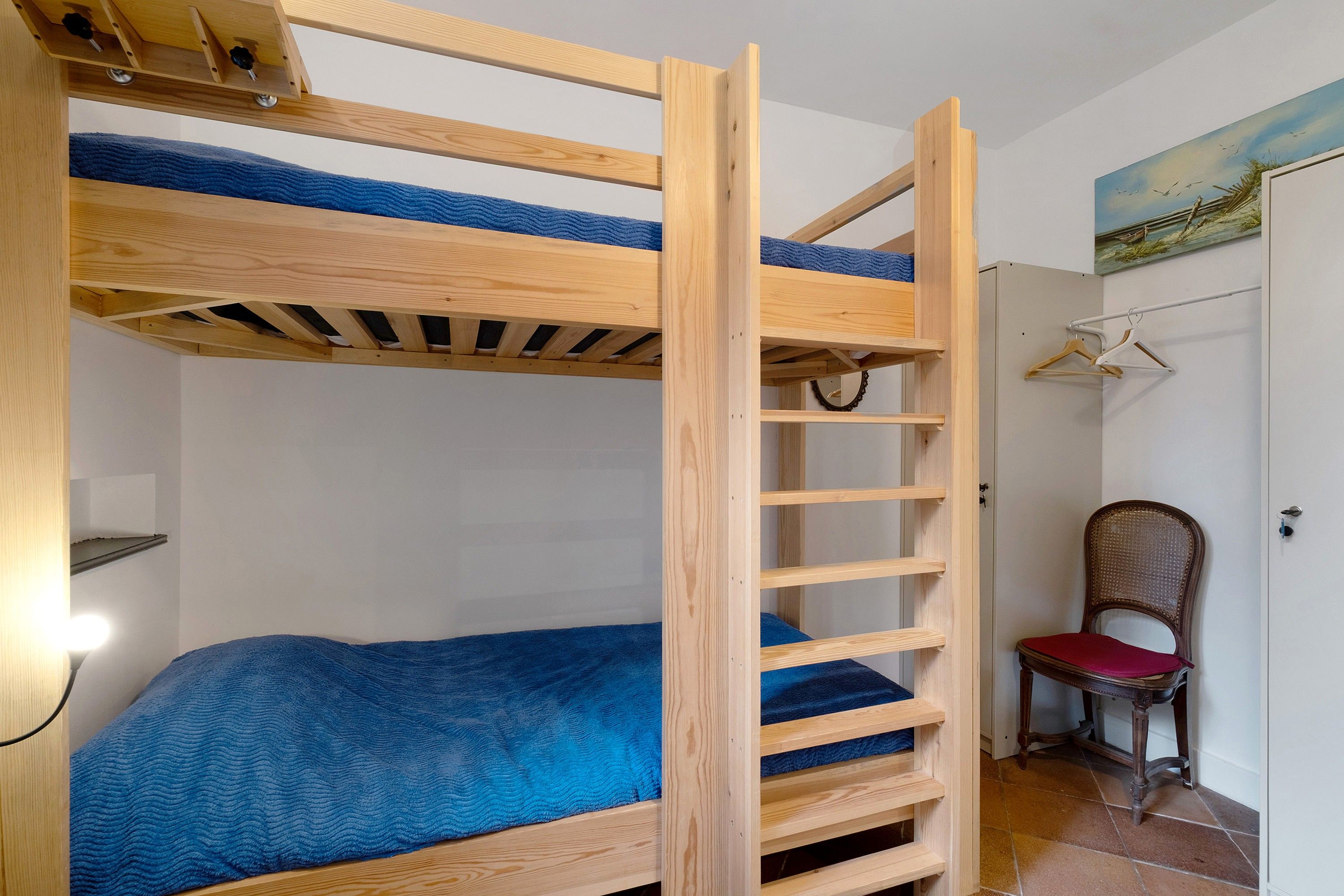 Una cama litera con escalera, una silla y un cuadro en la pared.