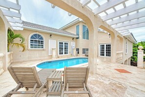 Ein überdachter Poolbereich im Freien mit Liegestühlen und einer Pergola.