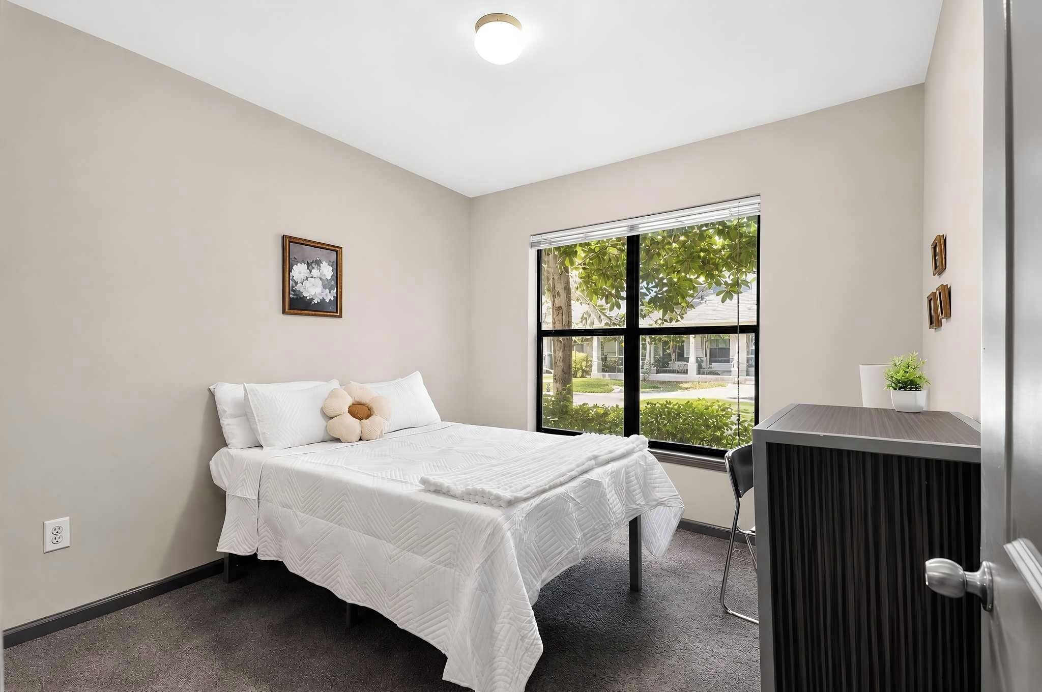 A bedroom with a bed, a window, a desk, and a chair.