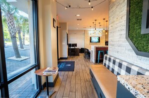 A modern interior with a reception desk, seating area, and a kitchen visible in the background.