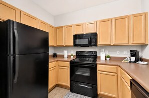 A kitchen with wooden cabinets, a black refrigerator, a microwave, a stove, and a coffee maker. - Balcony Retreat Near USC, The Vista & Downtown (Columbia)
