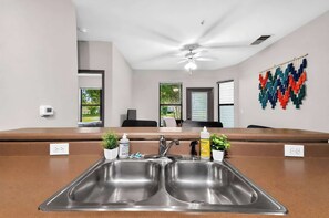 A modern kitchen with a double sink, a ceiling fan, and a view of the outside through large windows.