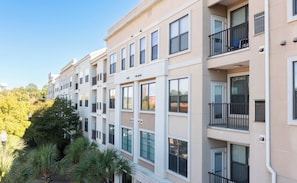 A multi-story residential building with balconies, large windows, and a surrounding lush green landscape.