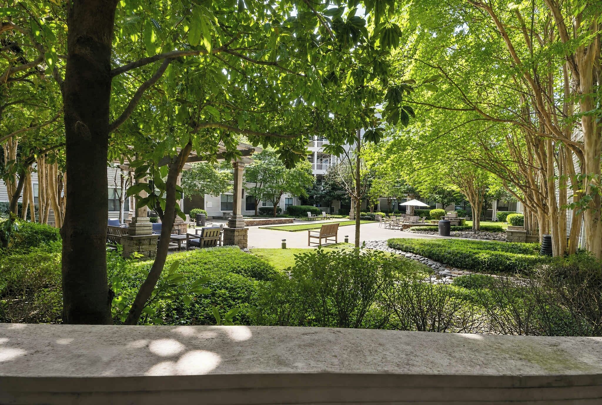 A courtyard with seating areas, a central lawn, and surrounding trees.