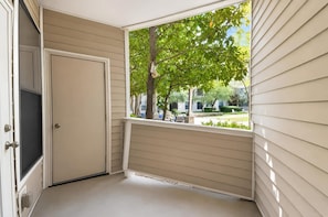A room with a door, a window with a view of a garden, and a ceiling with a light fixture.