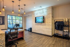 A modern office space with a large window, a television mounted on the wall, and a clothing rack with casual wear. - Balcony Retreat Near USC, The Vista & Downtown (Columbia)
