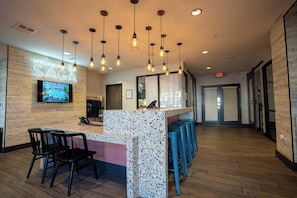 A hotel lobby with a reception desk, bar area, seating, and a TV screen displaying a pool view.