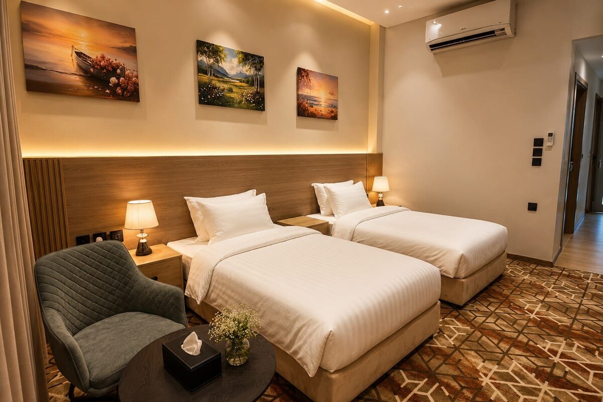 A hotel room with two beds, a chair, a small table, and artwork on the walls.