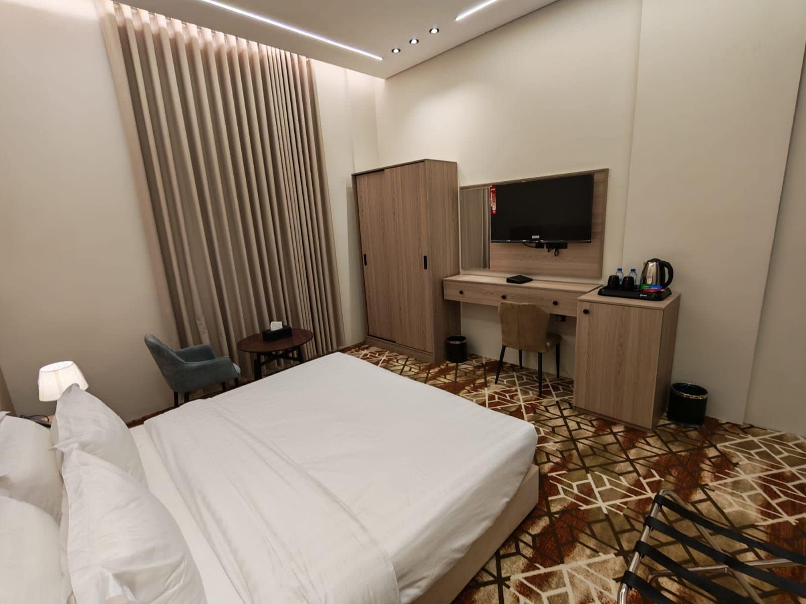 Hotellihuone, jossa on sänky, työpöytä, jossa on televisio, tuoli ja vaatekaappi.