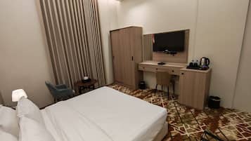 Una habitación de hotel con una cama, un escritorio con televisor, una silla y un armario.