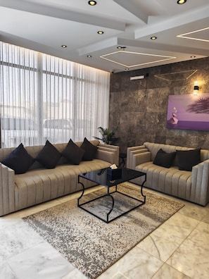 Una sala de estar moderna con dos sofás, una mesa de centro y un gran ventanal con cortinas translúcidas.