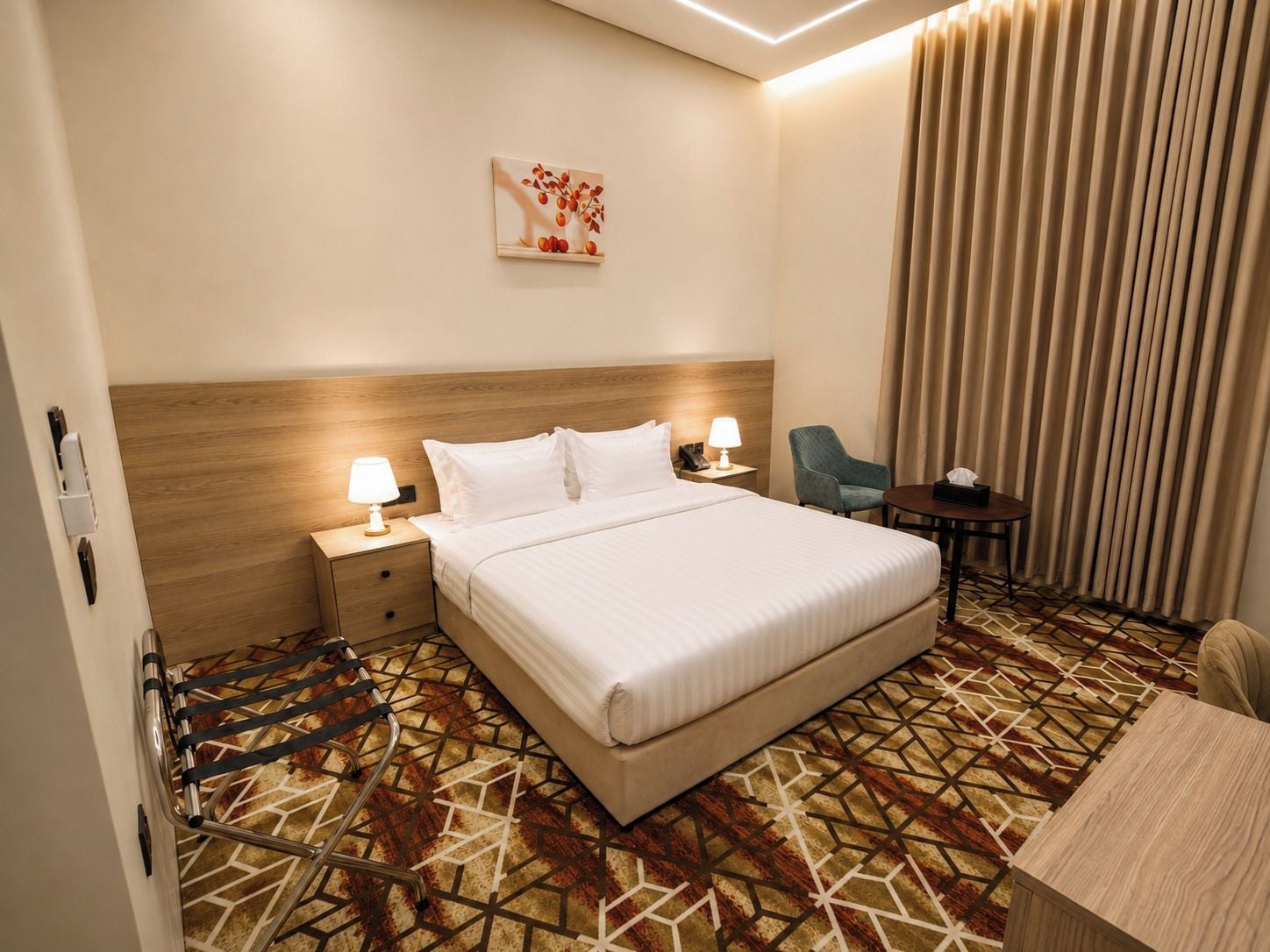 A hotel room with a large bed, bedside tables, a desk, a chair, and a patterned carpet.