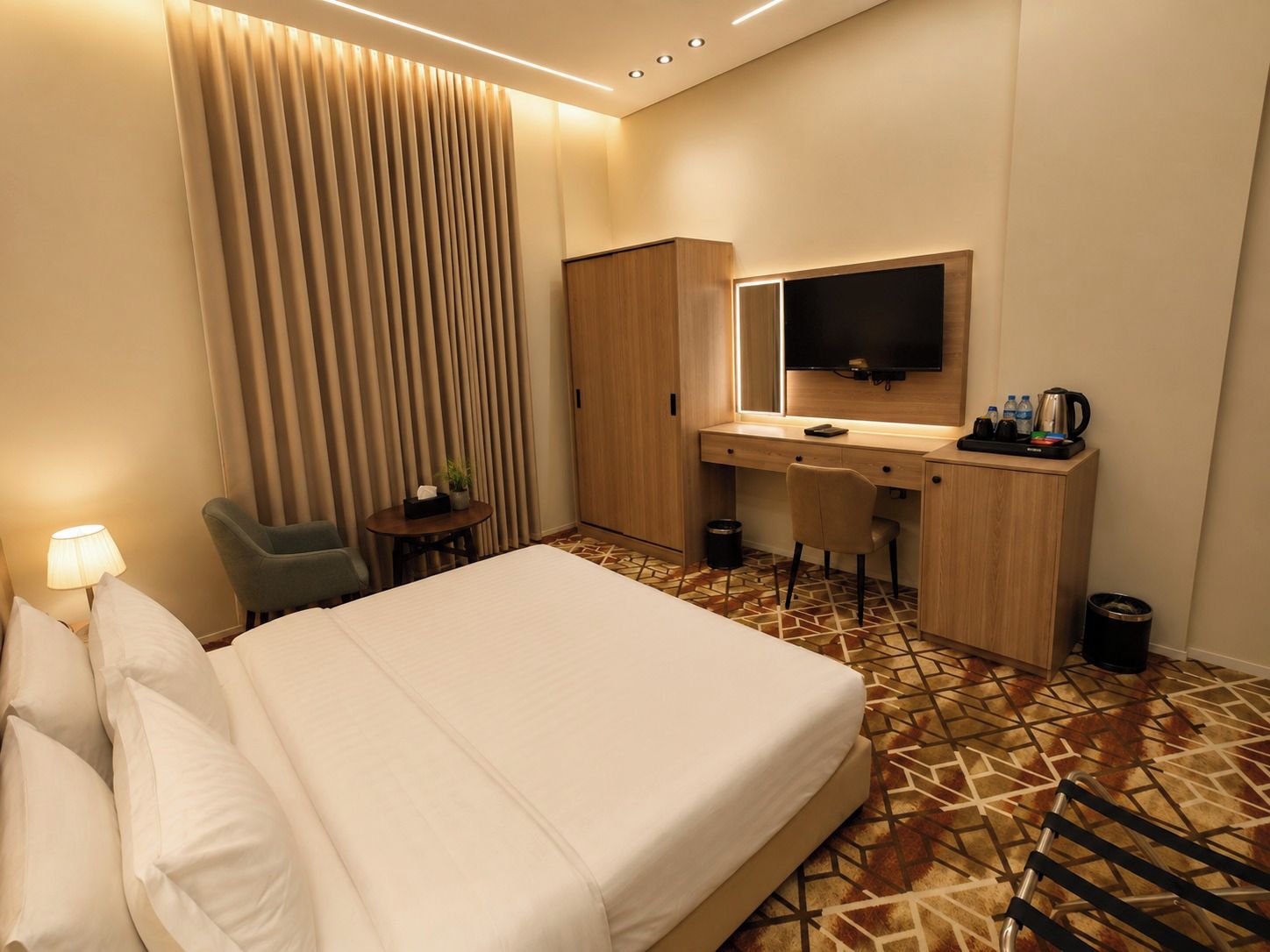 Une chambre d’hôtel équipée d’un lit, d’un bureau, d’une chaise, d’une télévision et d’une petite table sur laquelle est posée une plante.