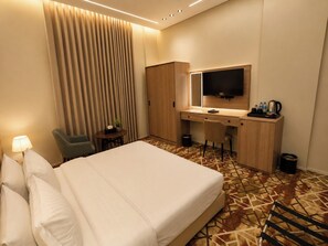 Habitación de hotel con cama, escritorio, silla, televisión y una mesita con una planta.