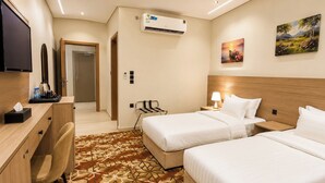 Ein Hotelzimmer mit zwei Betten, einem Schreibtisch, einem Stuhl, einem Fernseher, einer Klimaanlage und einem Gemälde an der Wand.