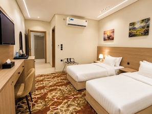A hotel room with two beds, a desk, a chair, a TV, an air conditioner, and a painting on the wall. - tamouh almuttahida hotels (madinah)