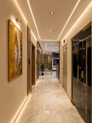 Un pasillo de hotel con piso de mármol, una recepción y una gran obra de arte con plumas en la pared.