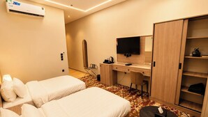 Ein Hotelzimmer mit zwei Betten, einem Schreibtisch, einem Flachbildfernseher, einem Kleiderschrank und einem kleinen Tisch mit einer Taschentuchbox.