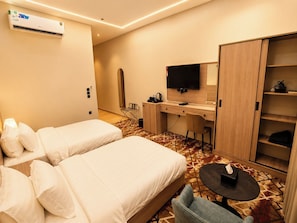 A hotel room with two beds, a desk with a flat-screen TV, a wardrobe, and a small table with a tissue box. - tamouh almuttahida hotels (madinah)