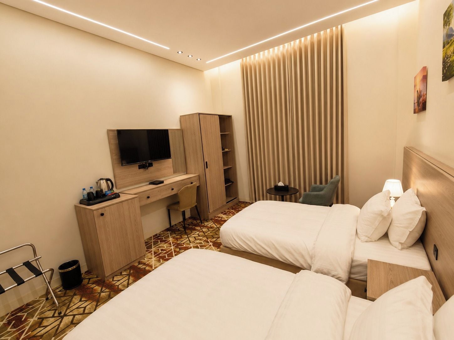 A hotel room with two beds, a desk with a television, and a large window with curtains.