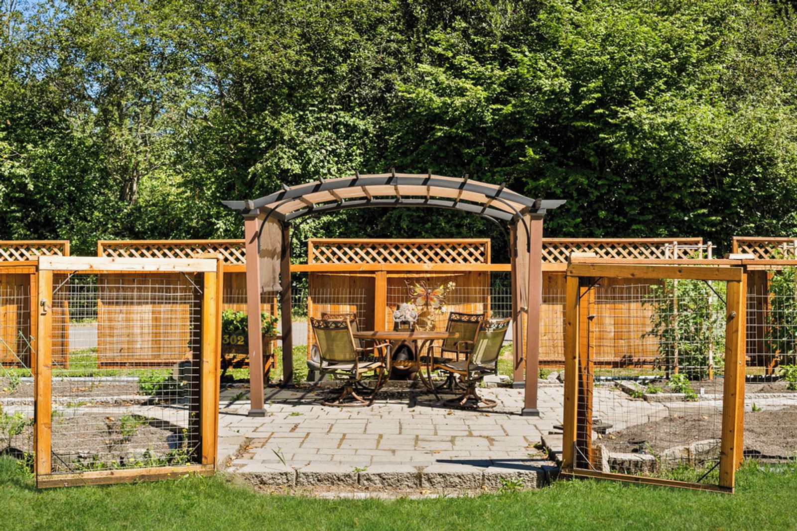 Puinen pergola, puutarhapatio, pöytä ja tuolit sekä aidattu alue, jossa näkyy numero 302.