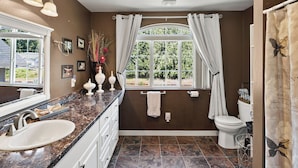 Une salle de bain avec un plan de toilette en marbre, un lavabo blanc, des toilettes et une fenêtre avec des rideaux.